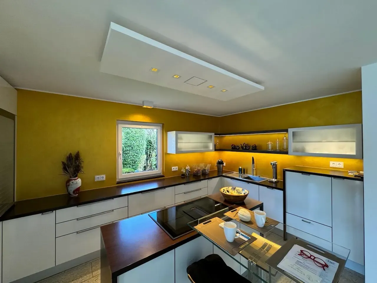 Luxuriöse Küche mit goldener Wandgestaltung und modernen Einbauten. Die Kombination aus weißen Schränken, einer großzügigen Arbeitsfläche und goldenen Wänden verleiht dem Raum Eleganz und Wärme. Diese hochwertige Renovierung wurde von farbDESIGN und WERKstatt umgesetzt und besticht durch ihr stilvolles Design und ihre durchdachte Lichtgestaltung.