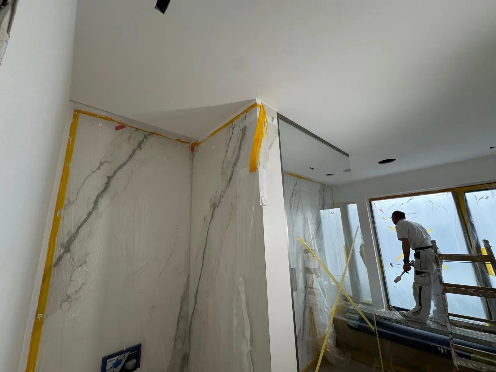 Handwerker arbeitet in einem modernen Neubau-Badezimmer mit großformatigen Marmoroptik-Fliesen und Glaswänden.