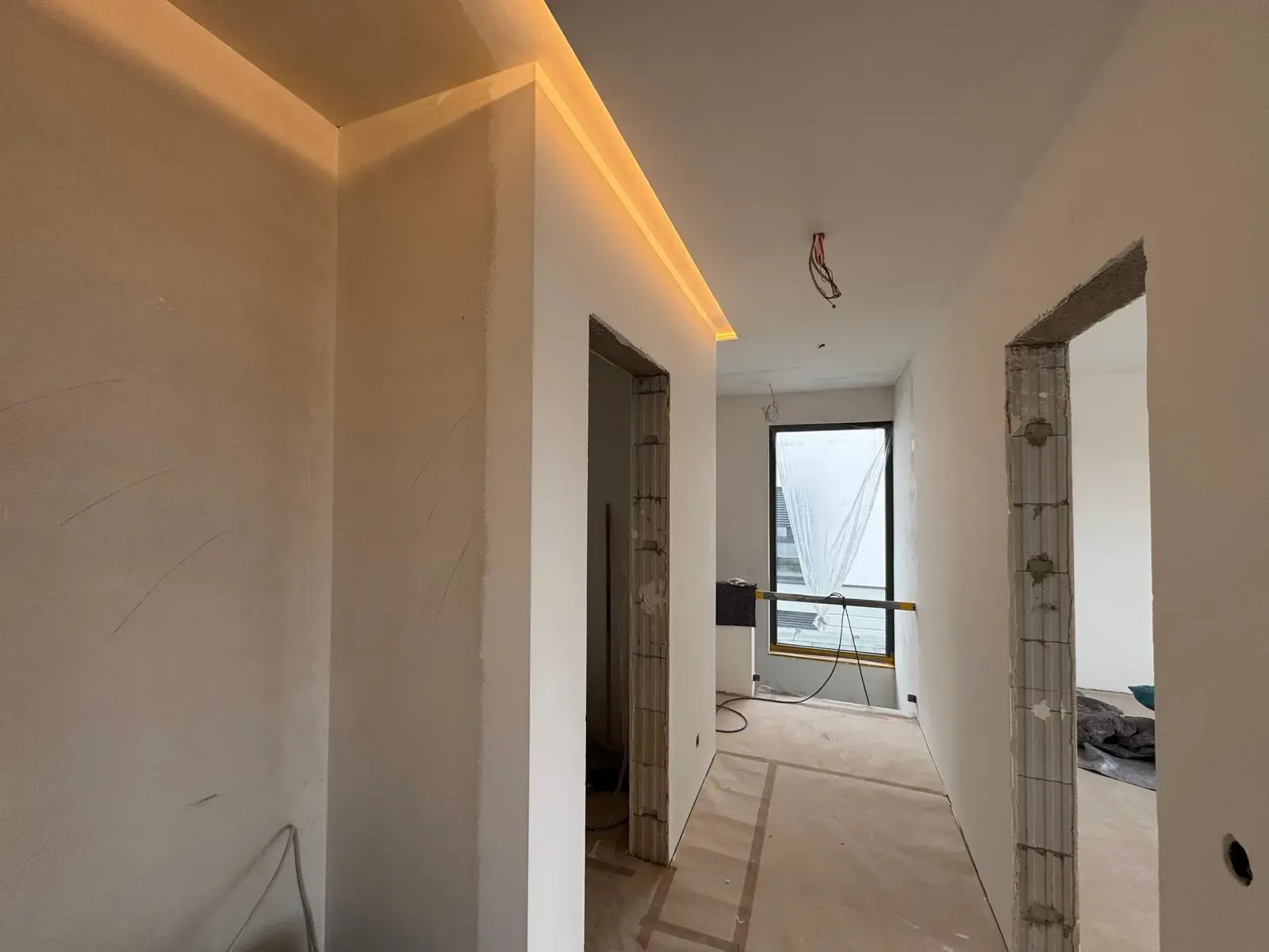 Rohbau-Flur mit moderner LED-Deckenbeleuchtung und offenen Türrahmen.