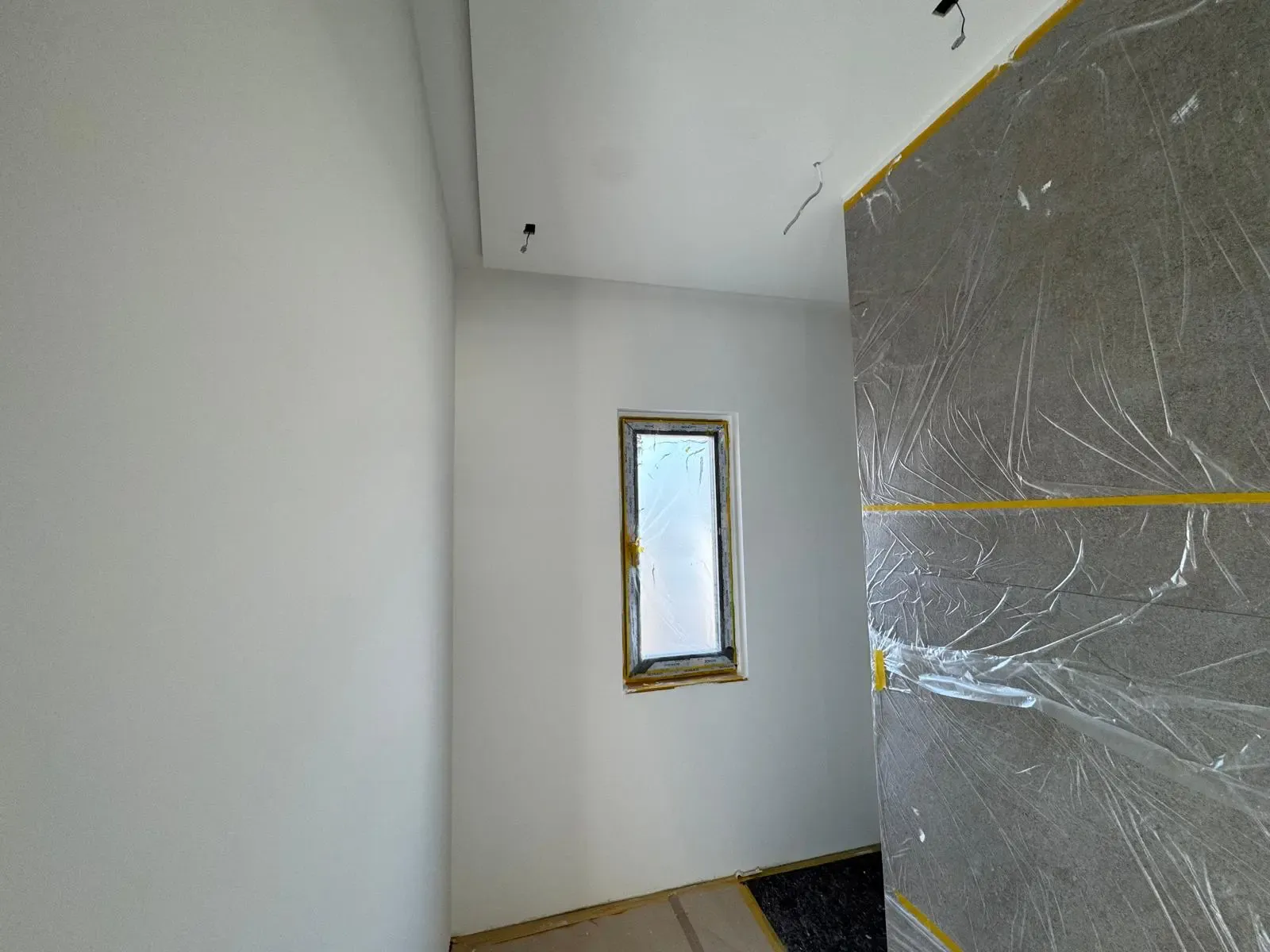 Frisch gespachtelte und grundierte Wand in einem Neubau, mit abgedeckter Fläche für Fliesenarbeiten.