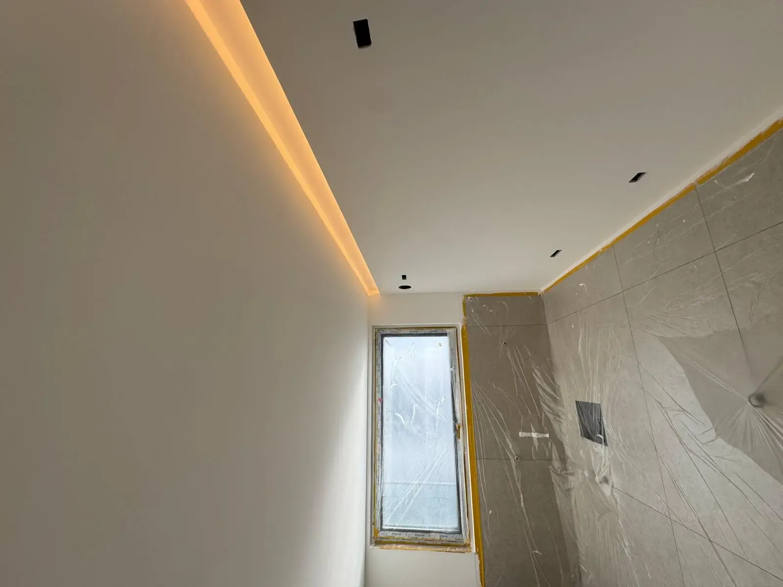 Teilweise fertiggestelltes Badezimmer mit LED-Lichtleiste an der Decke und großflächigen Fliesen.