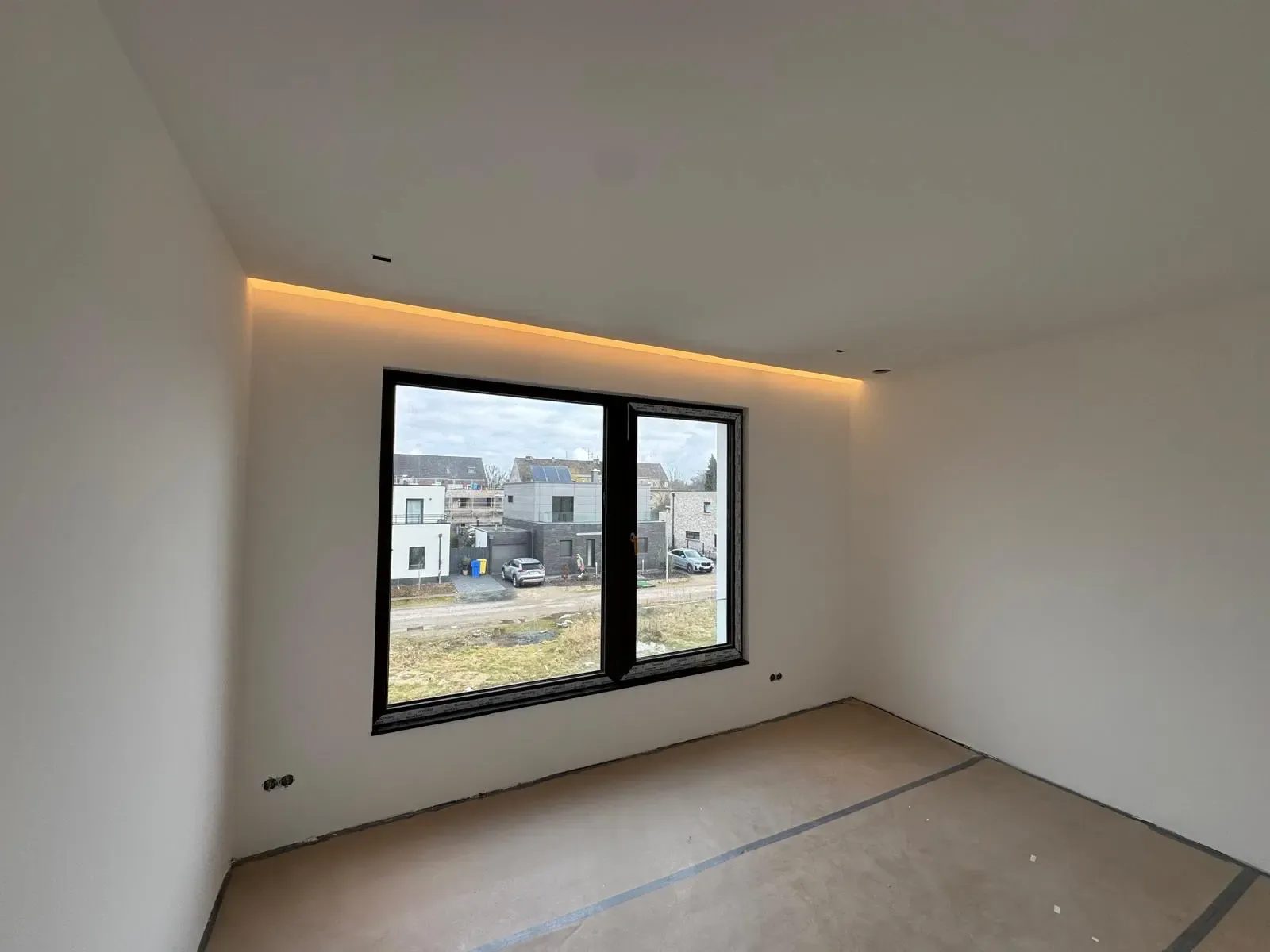 Minimalistisches Schlafzimmer im Rohbau mit LED-Deckenbeleuchtung und großem Fenster.