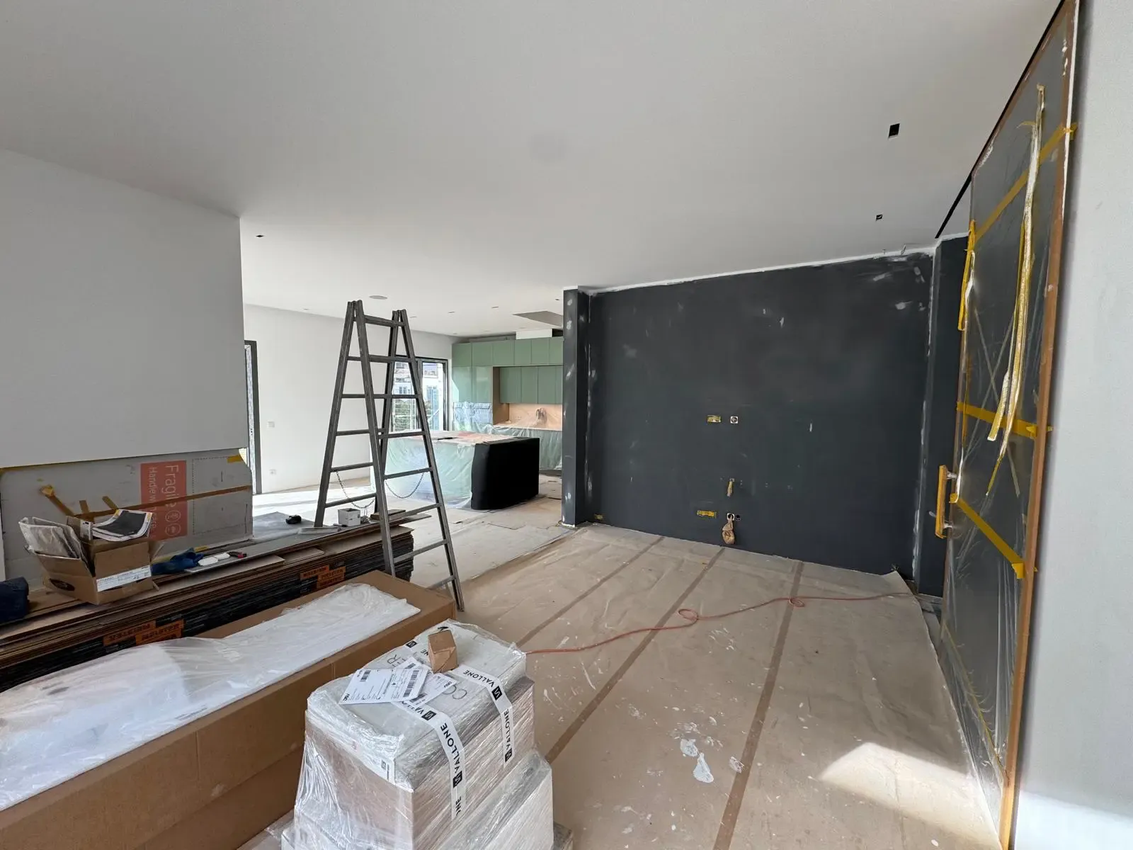 Baustelle einer modernen Wohnküche mit dunkler Akzentwand und grünen Küchenschränken.