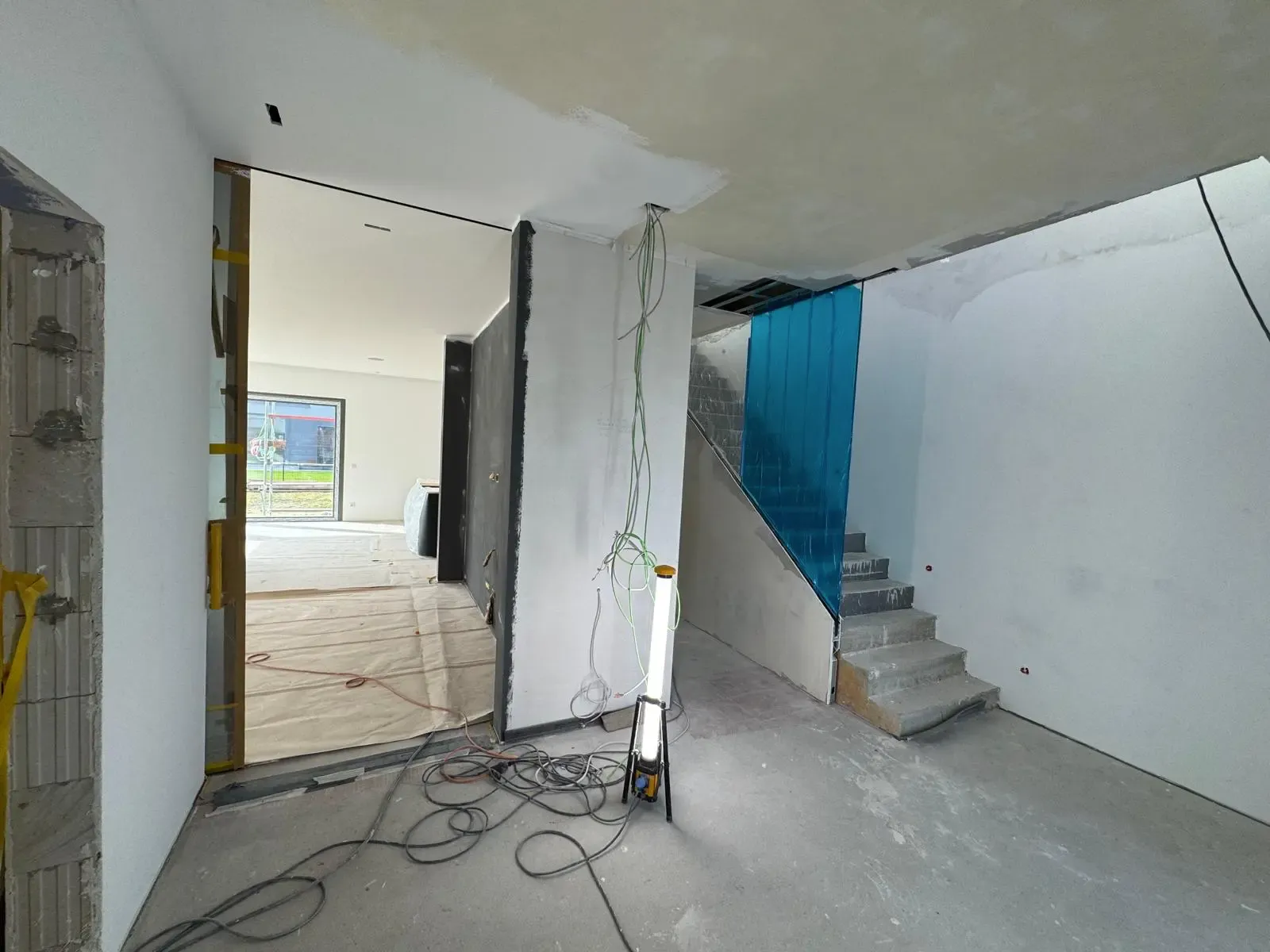 Unfertiger Innenbereich eines Neubaus mit Beton-Treppe, offener Verkabelung und Schutzfolie.