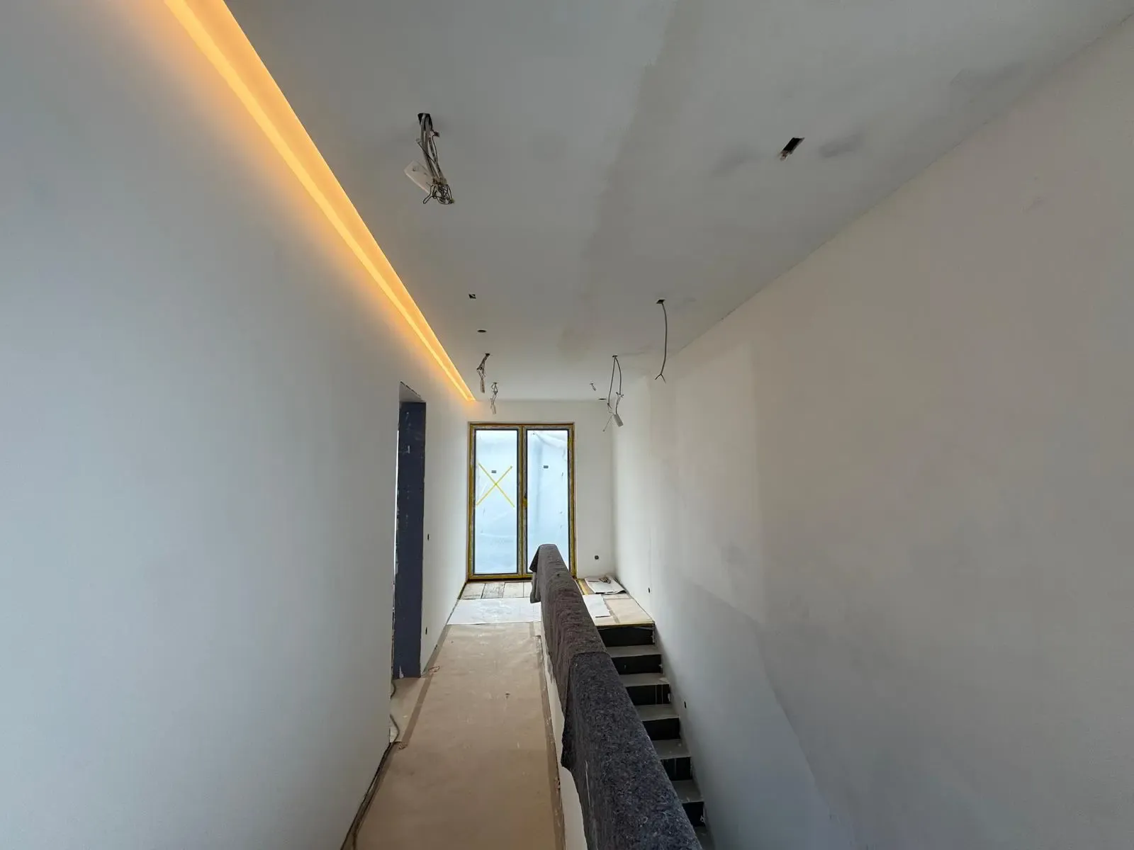 Rohbau-Treppenaufgang mit indirekter LED-Beleuchtung entlang der Decke.