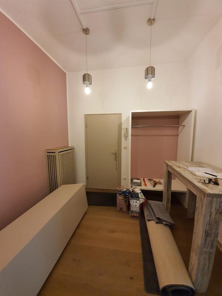 Praxis im Renovierungsprozess mit rosa Wand und Bodenschutz während der Malerarbeiten.
